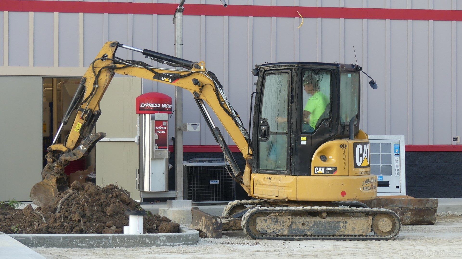 Yellow excavator moving dirt near a building, operator inside the cab.