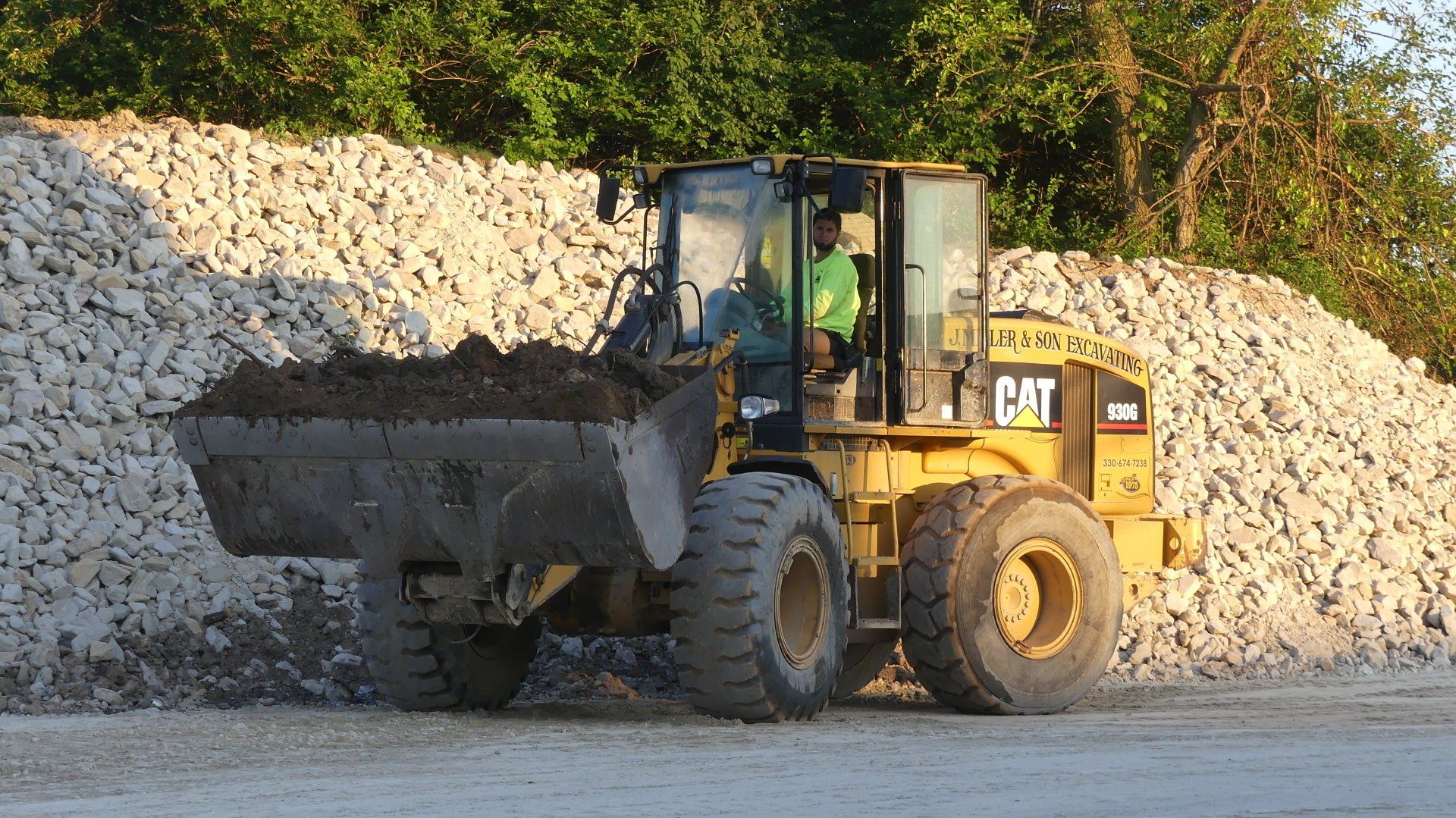 Yellow Caterpillar loader scoops dirt near large rock pile.