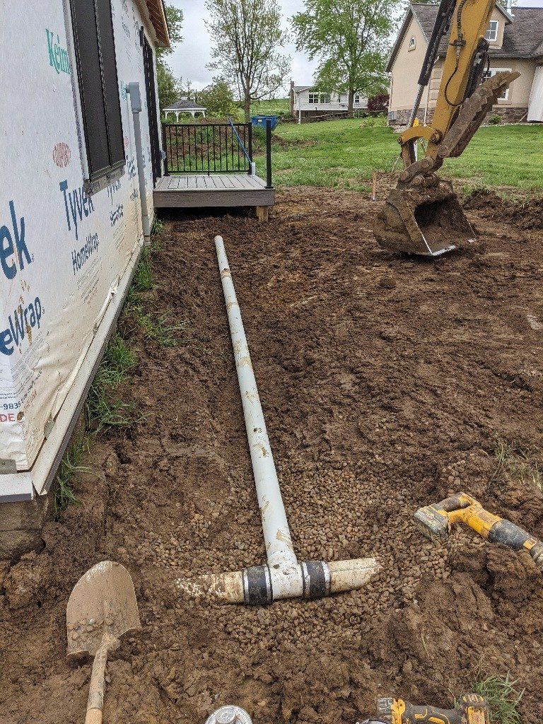 Construction site: PVC pipe extending from a building, excavator, shovel, and muddy ground.