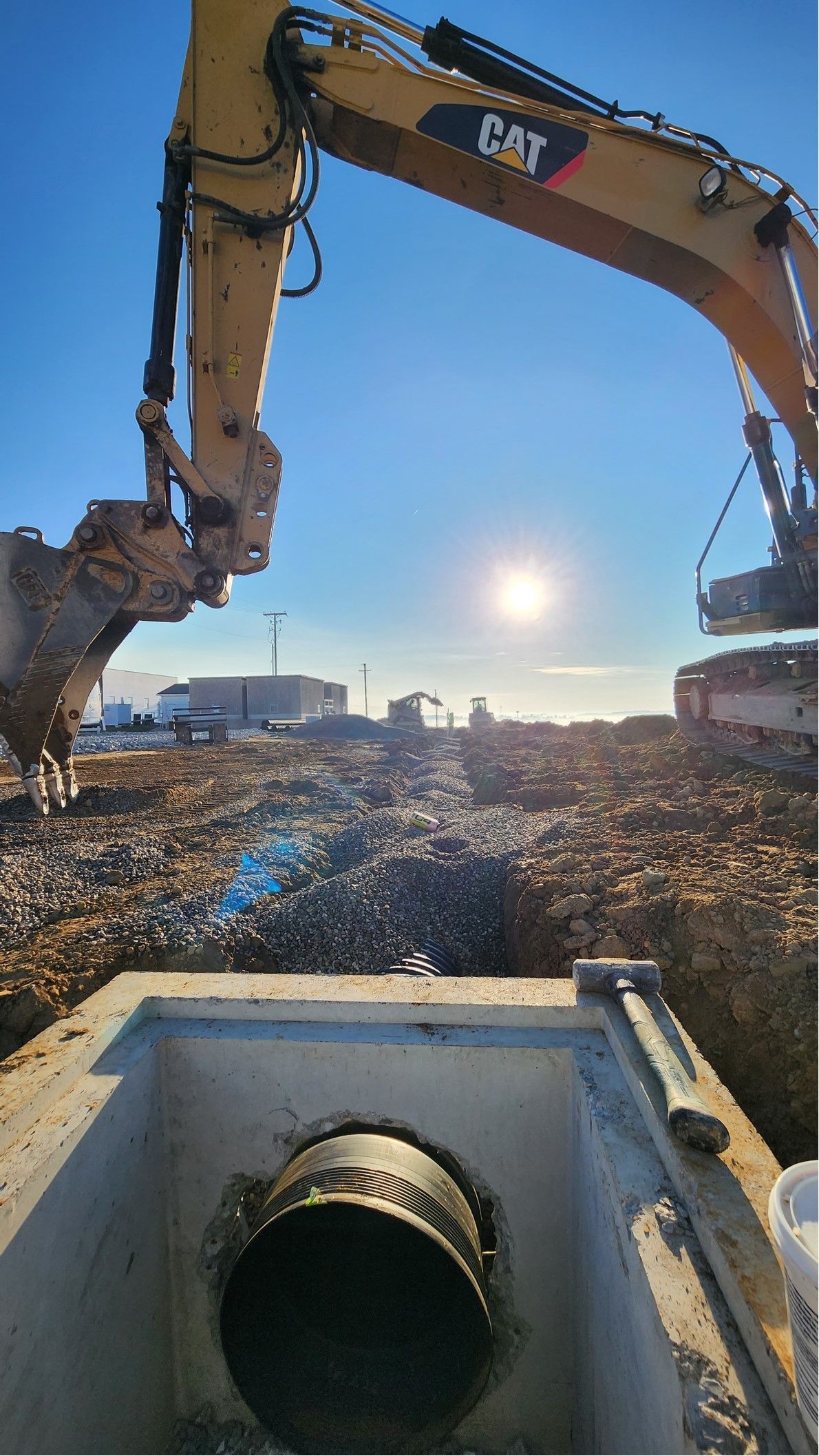 An excavator works at a construction site, sunny day. Pipe visible in concrete.