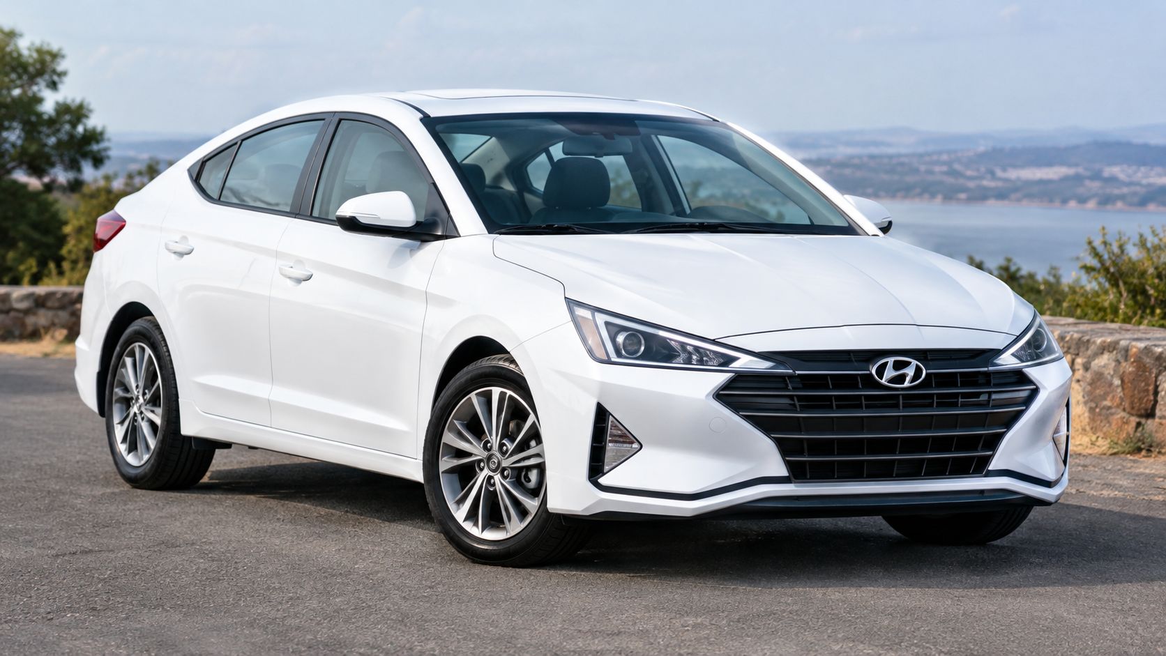 White Hyundai sedan parked on a roadside with a scenic water view in the background