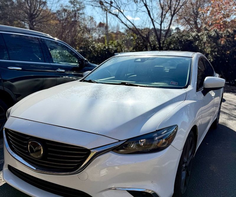 A white Mazda sedan parked outdoors next to a dark SUV on a sunny day.