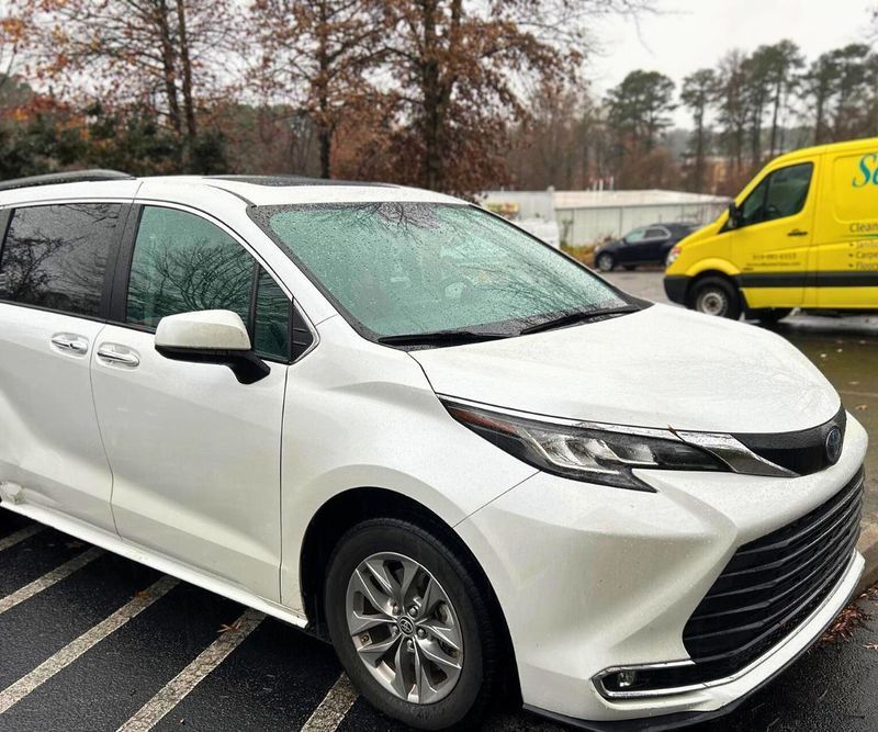A white minivan parked in an outdoor parking lot with a yellow van in the background.