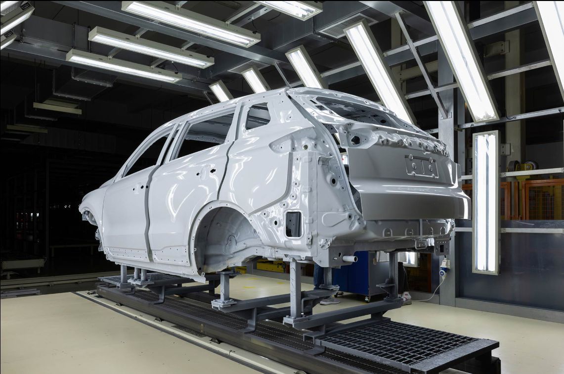 White car body on an assembly line in a factory, under bright overhead lights.