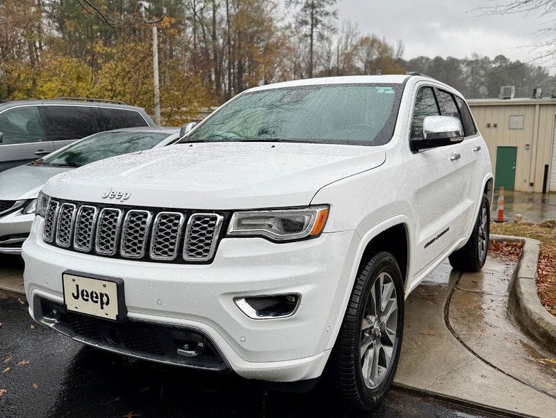 A white Jeep Grand Cherokee parked in a lot on a cloudy, rainy day.