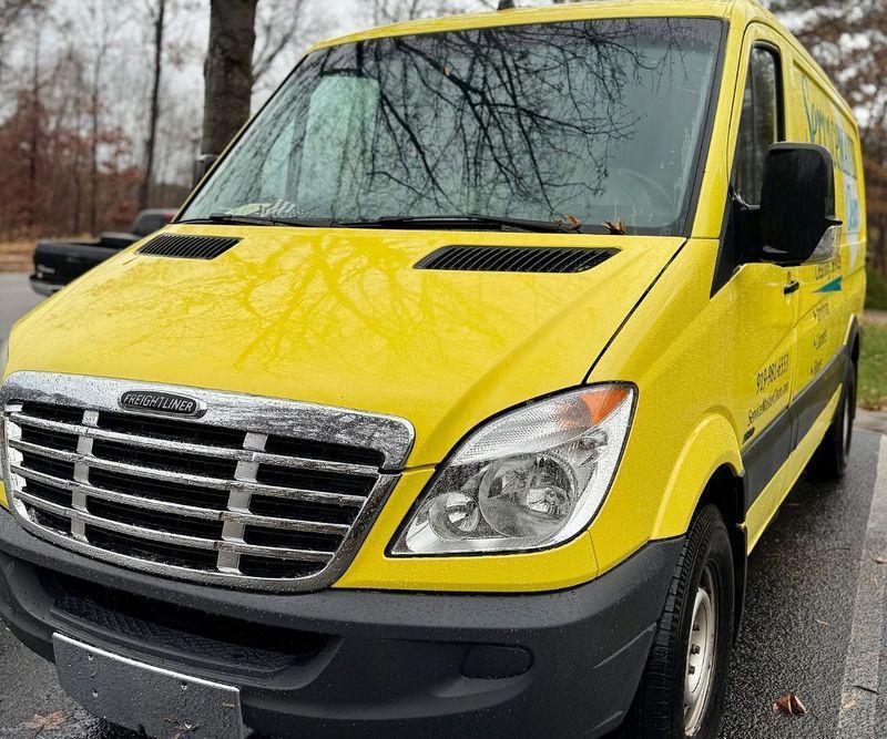 A bright yellow Freightliner cargo van parked outdoors on an overcast day.