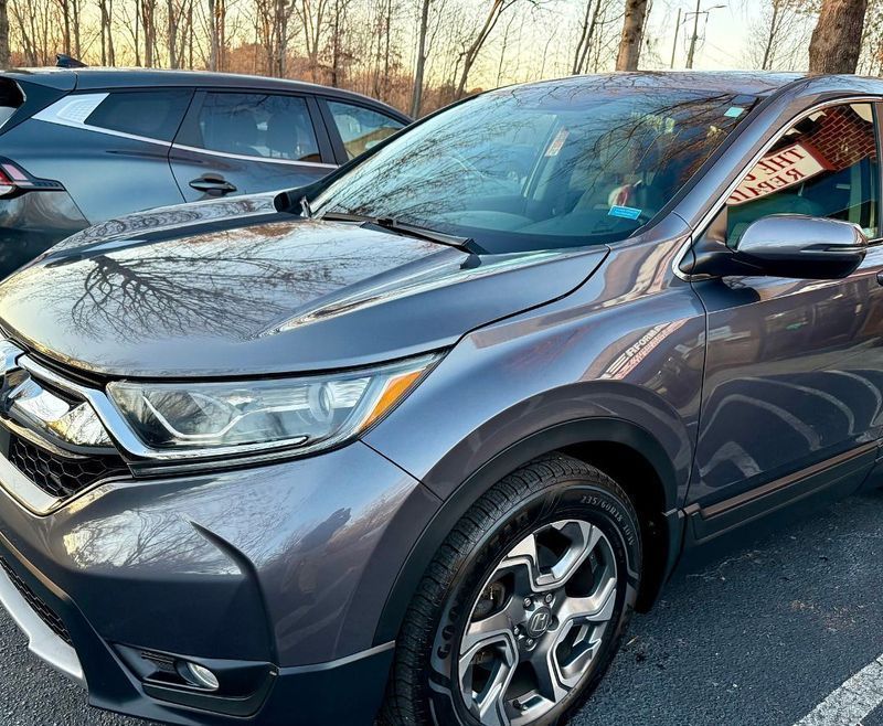 A grey Honda CR-V parked outdoors during sunset, with another car partially visible in the background.