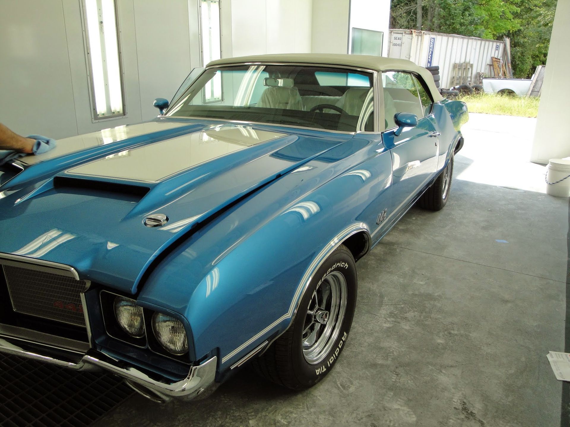 A metallic blue vintage convertible car with a white racing stripe parked inside a bright workshop.