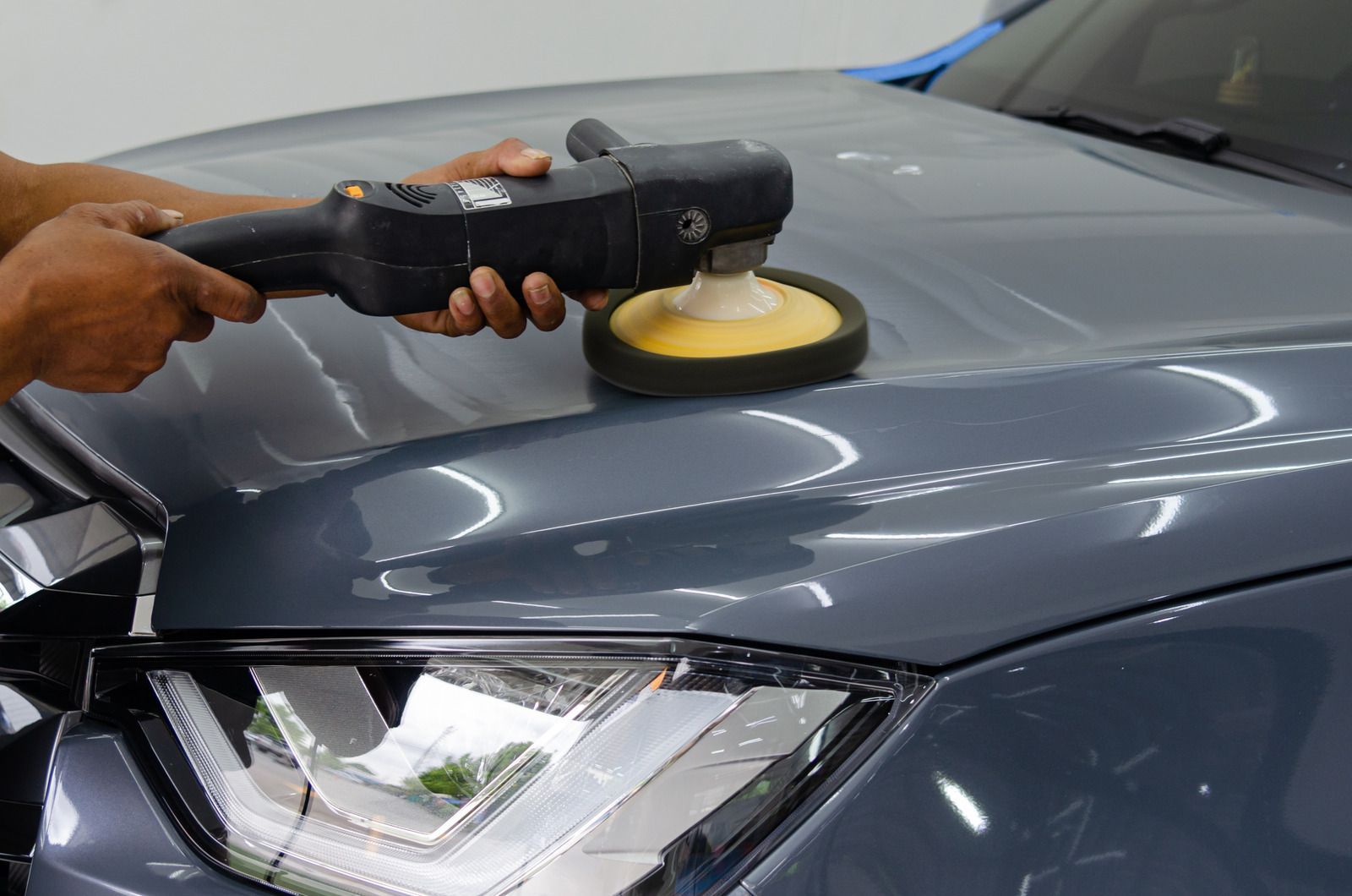 A clean, indoor auto repair shop with a dark blue car on a lift and a white car parked on a floor ramp.
