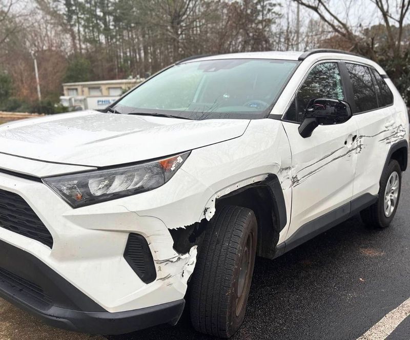A white Toyota RAV4 with significant damage to the front bumper, wheel arch, and side panels.