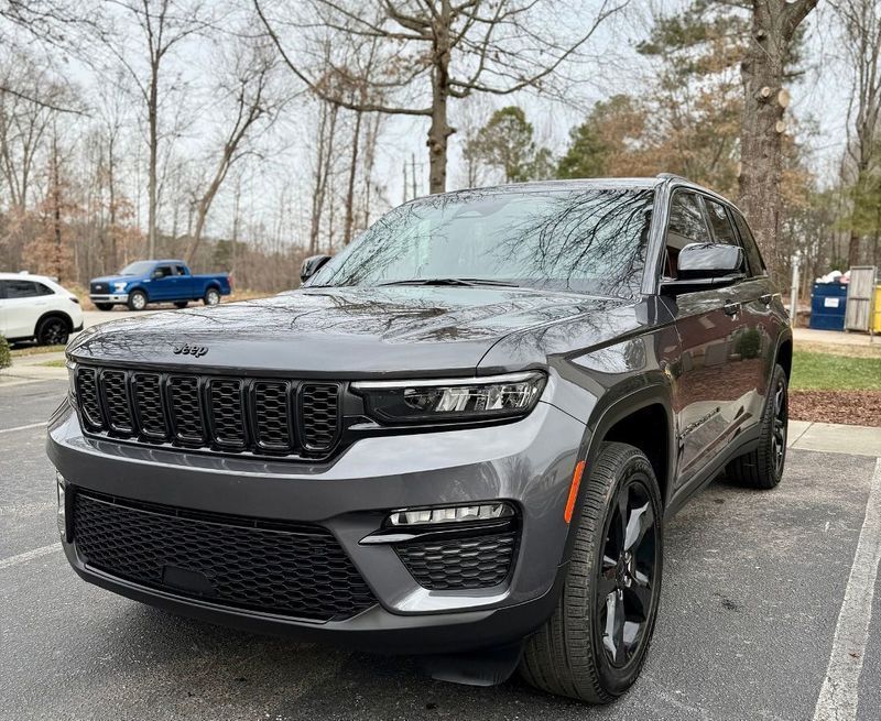 A grey Jeep Grand Cherokee parked in a lot with a blue pickup truck in the background.