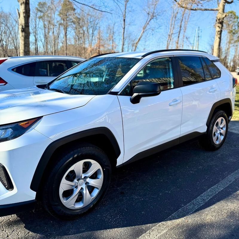 A white Toyota RAV4 SUV parked outdoors in a sunny area next to another vehicle.