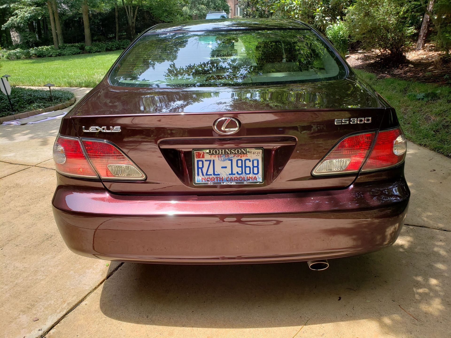 A dark burgundy Lexus LS 430 sedan parked on a concrete driveway with green trees and grass in the background.