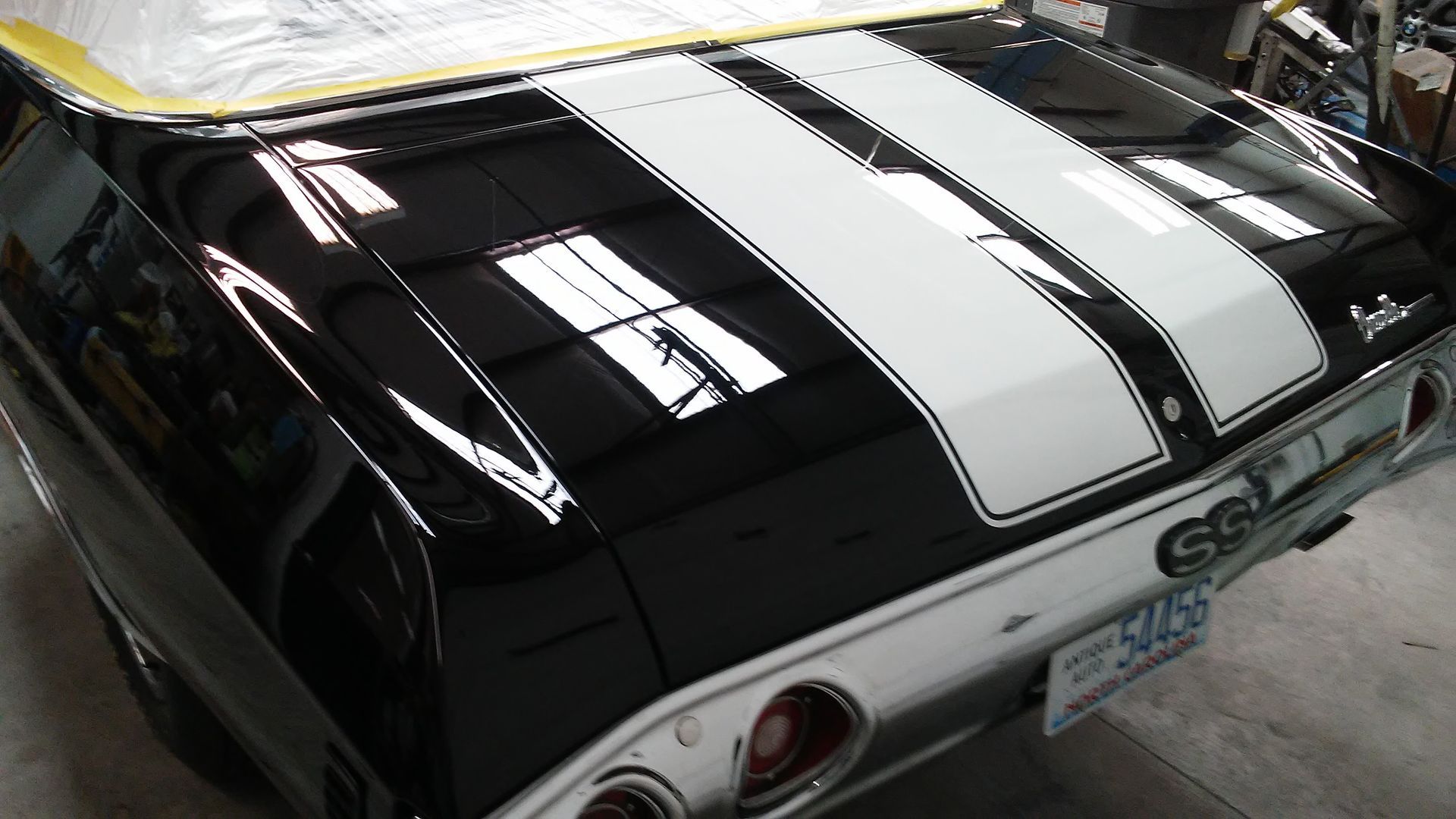 The rear view of a black classic Chevrolet Chevelle SS with dual white racing stripes on the trunk in a workshop.