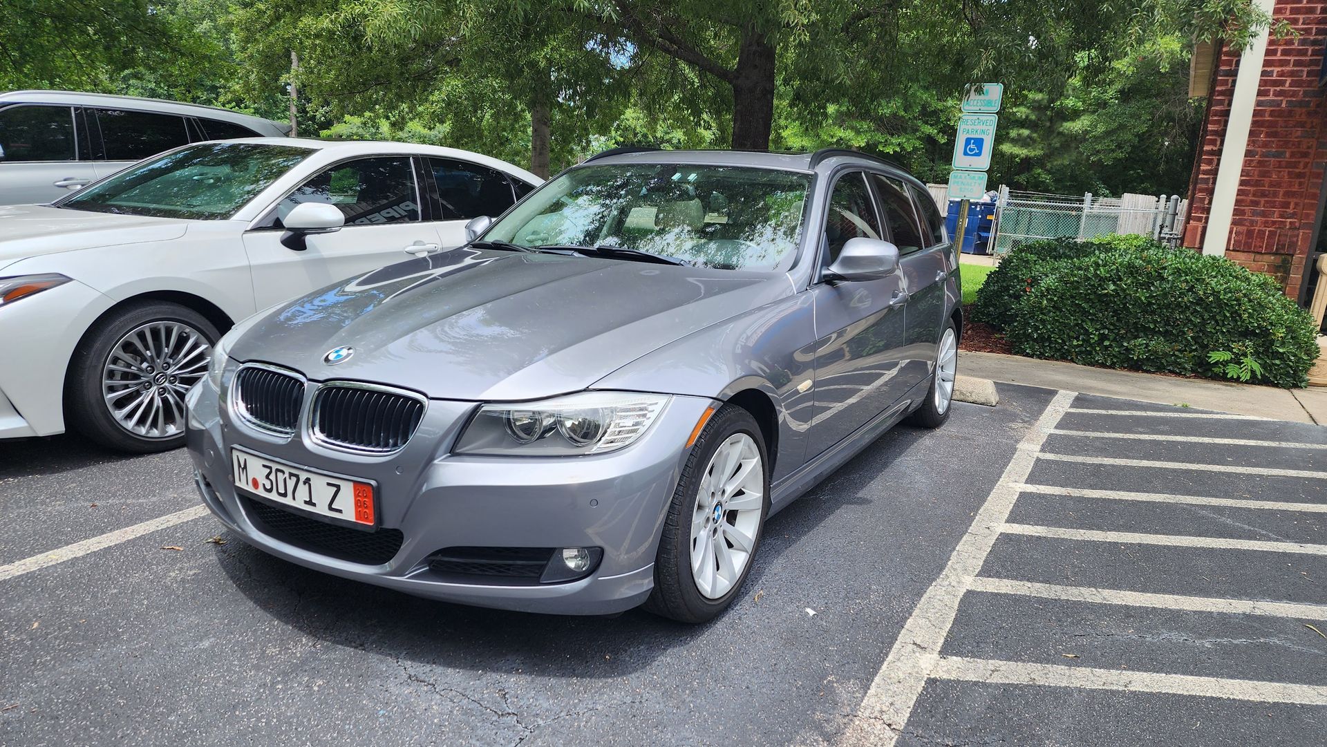 A silver BMW station wagon parked in a paved lot next to a white car on a sunny day.