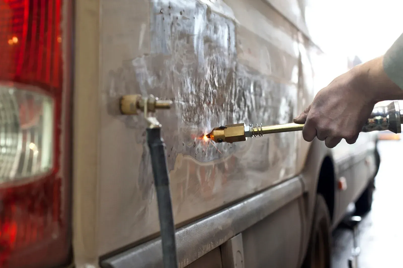 A person uses a specialized dent repair tool to fix a small blemish on the white panel of a car.
