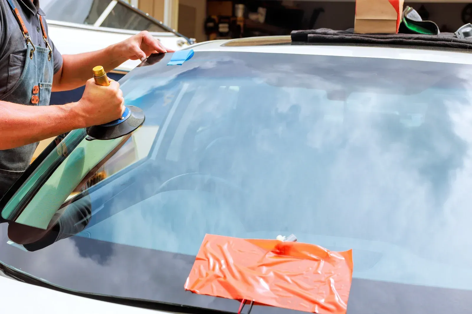 A technician using a suction cup tool to carefully position a new car windshield on a vehicle.