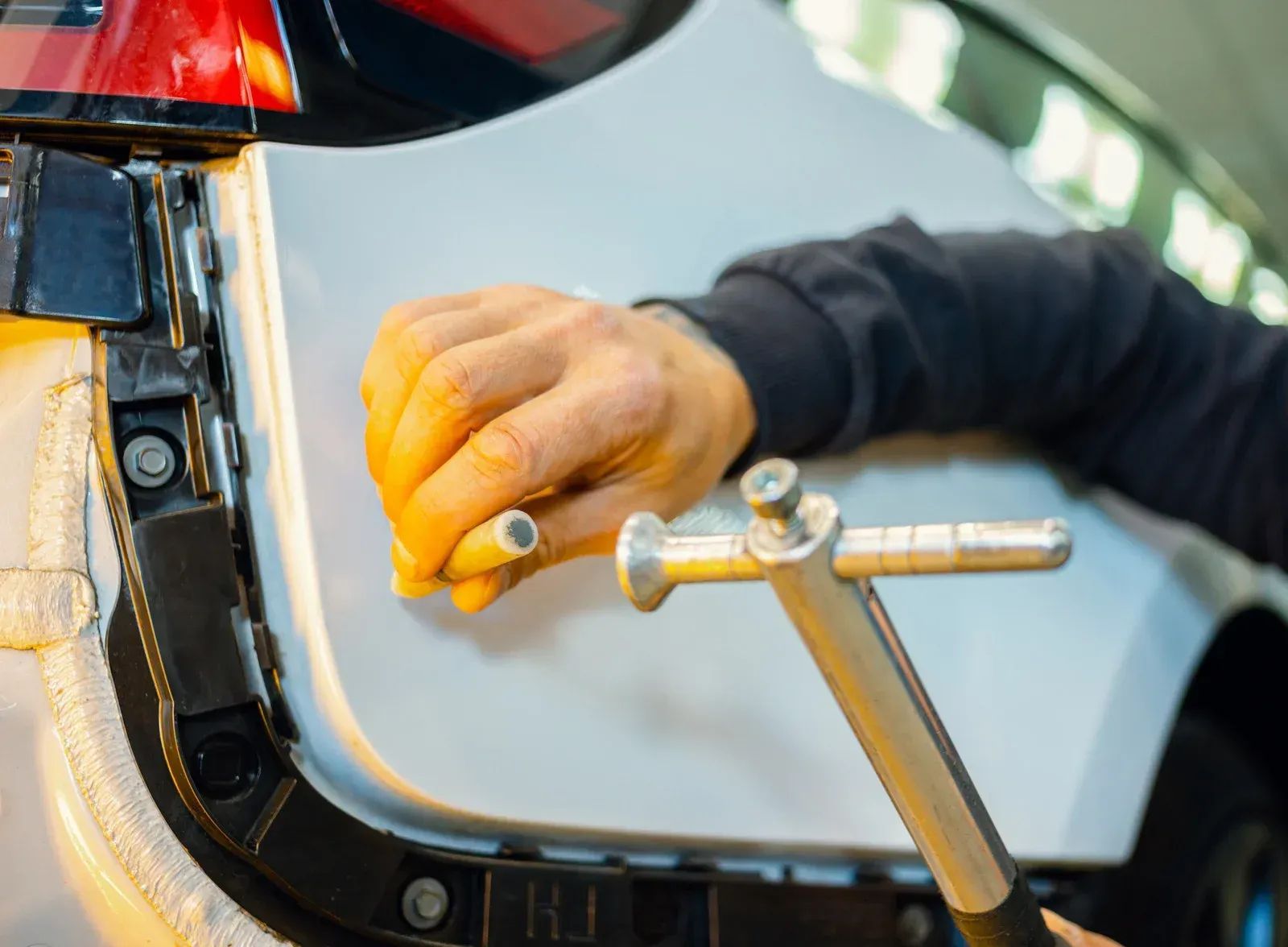 Hands using a wrench to repair a white car near the rear bumper