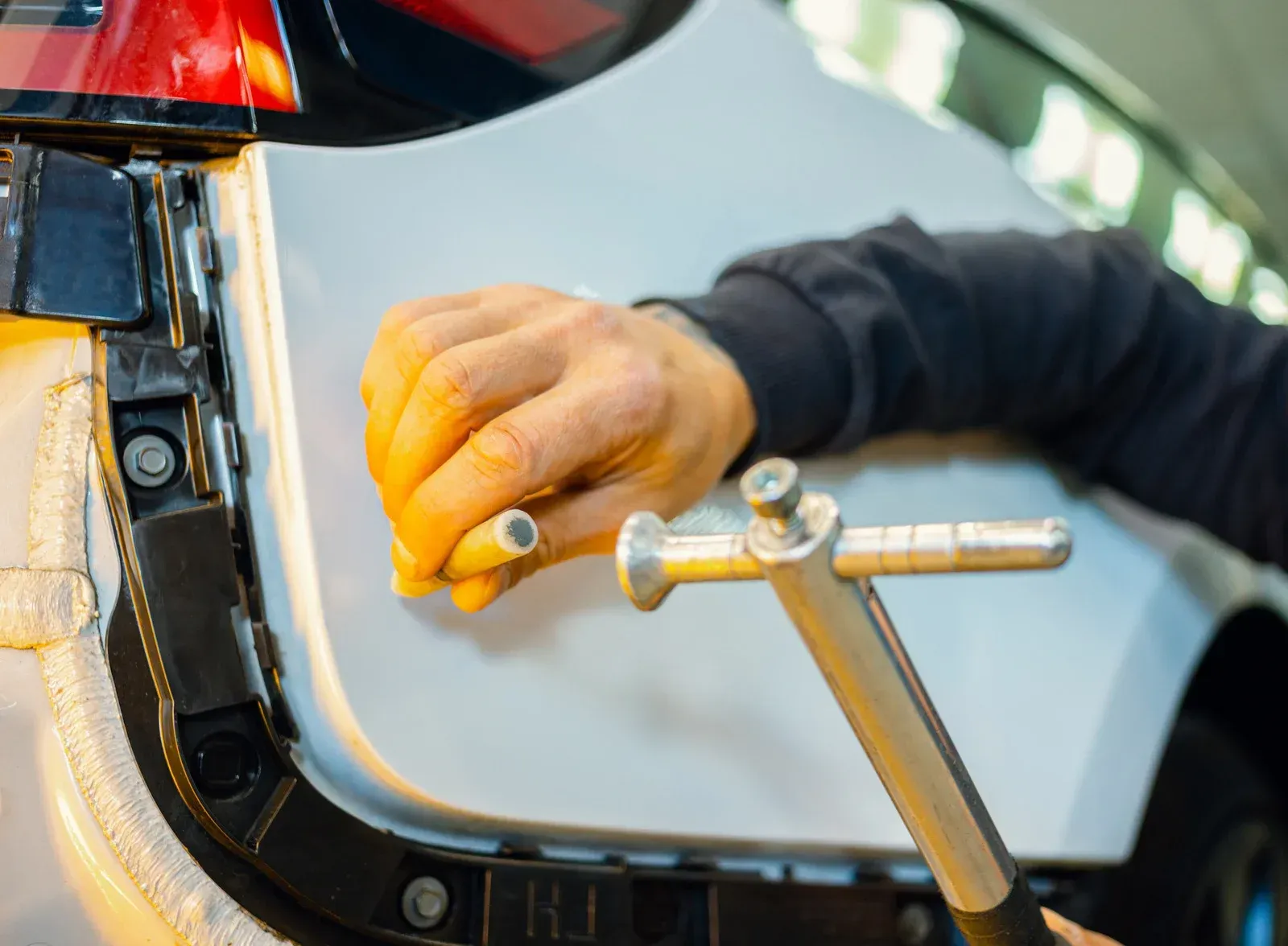 A technician uses a tool to perform paintless dent repair on the white panel of a vehicle.