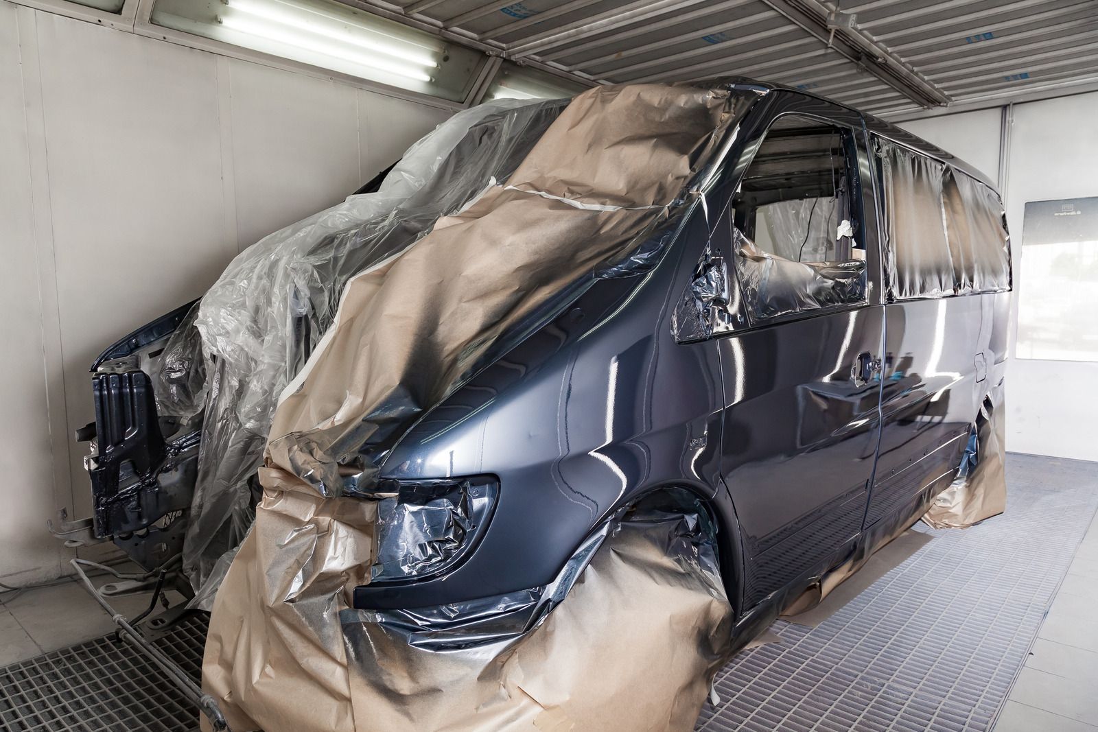 A professional technician in a garage polishes the hood of a red car using a mechanical buffer.