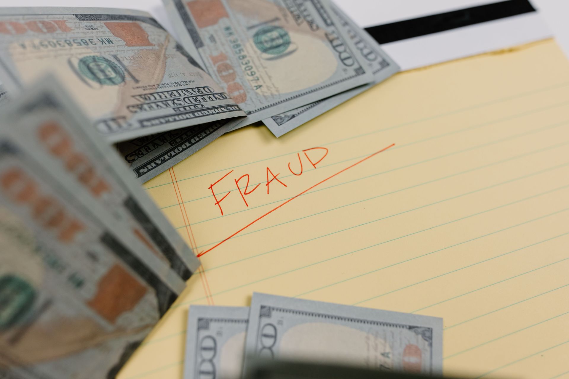 Stacks of cash beside a yellow notepad labeled “FRAUD” in red handwriting.