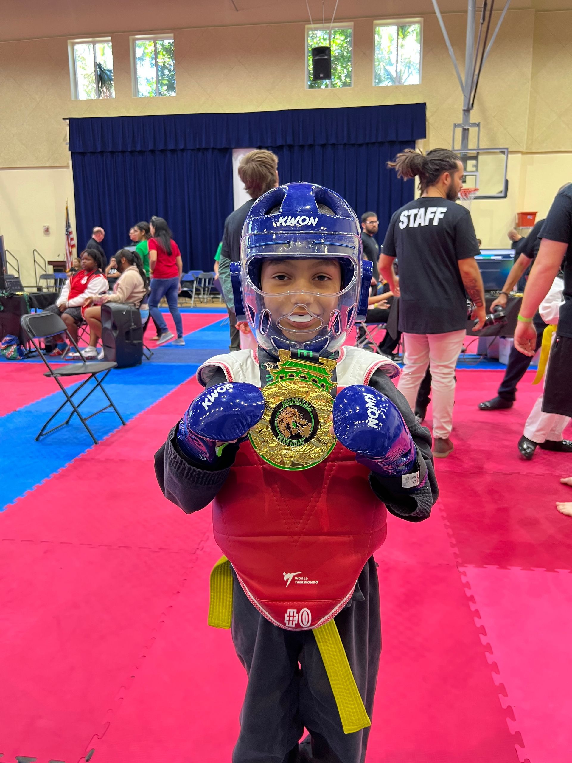 A young boy in a taekwondo uniform is holding a medal.