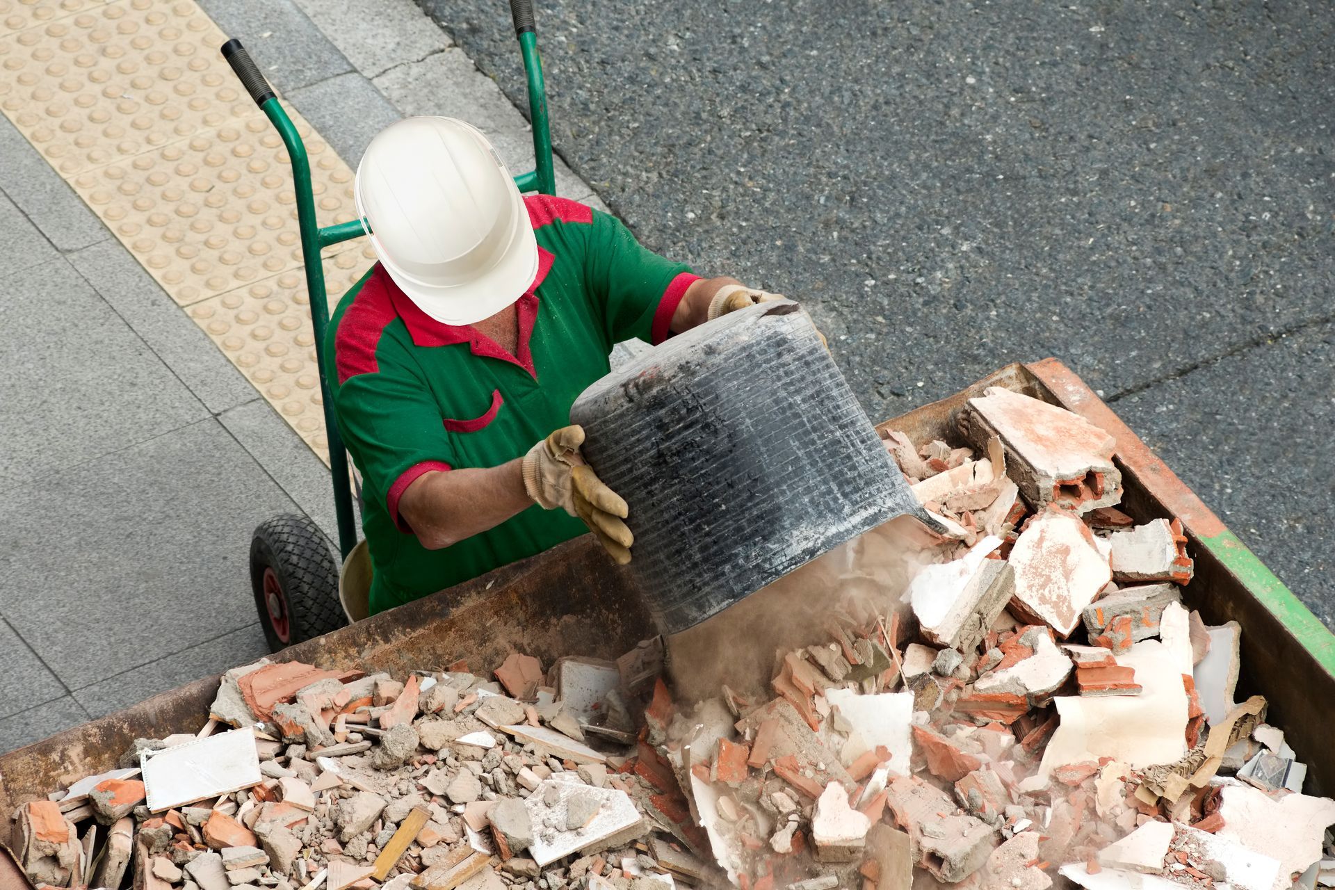 Bricklayer loading debris, showcasing junk removal services, furniture and tiles in city dumpster.