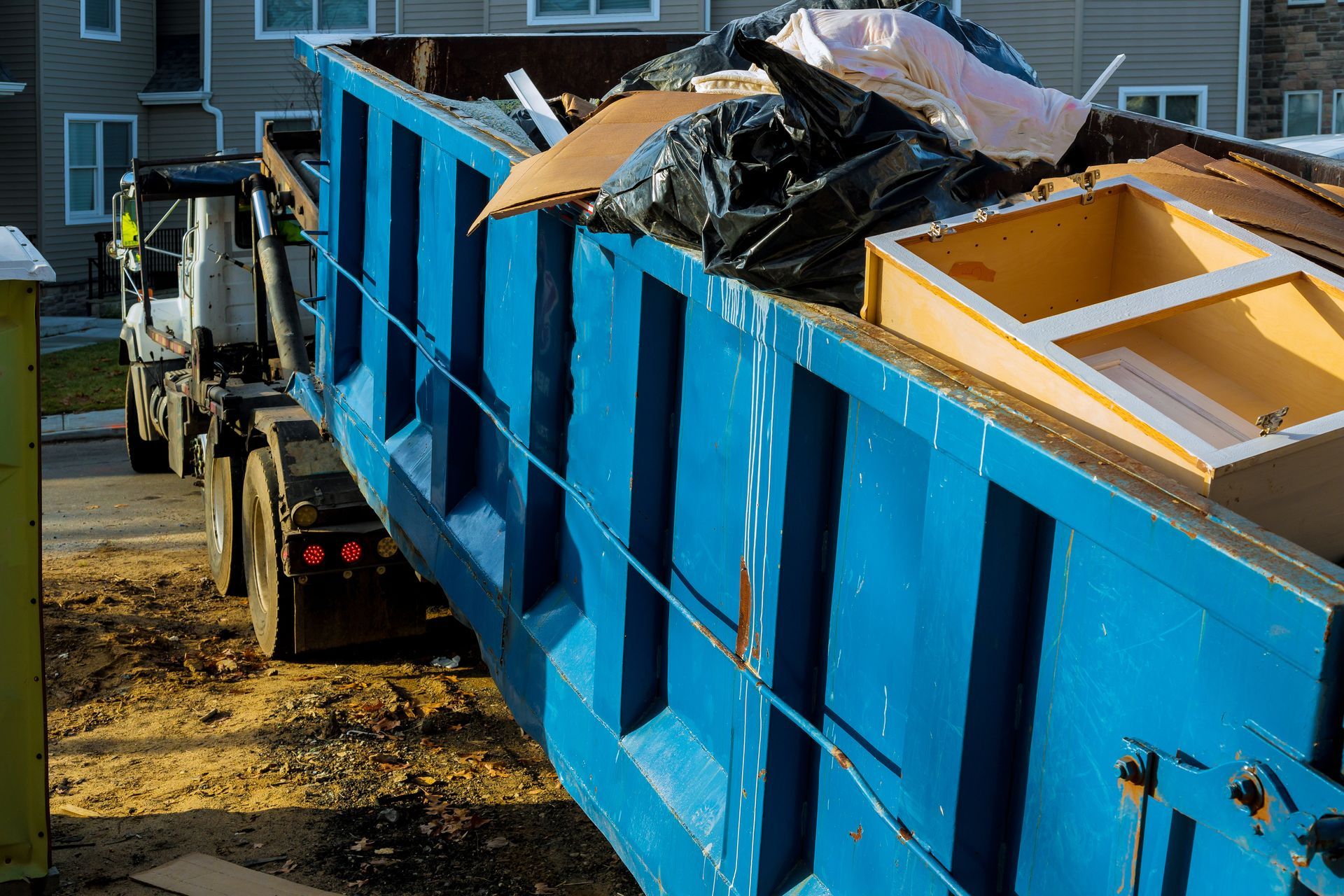 Large blue dumpster filled with debris being hauled by a truck at a job site. Large blue dumpster filled with debris being hauled by a truck at a job site.