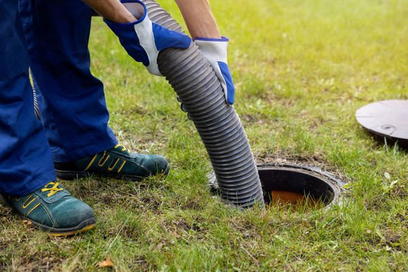 A Worker inserts a hose into an open septic tank on a grassy field. A Worker inserts a hose into an open septic tank on a grassy field.
