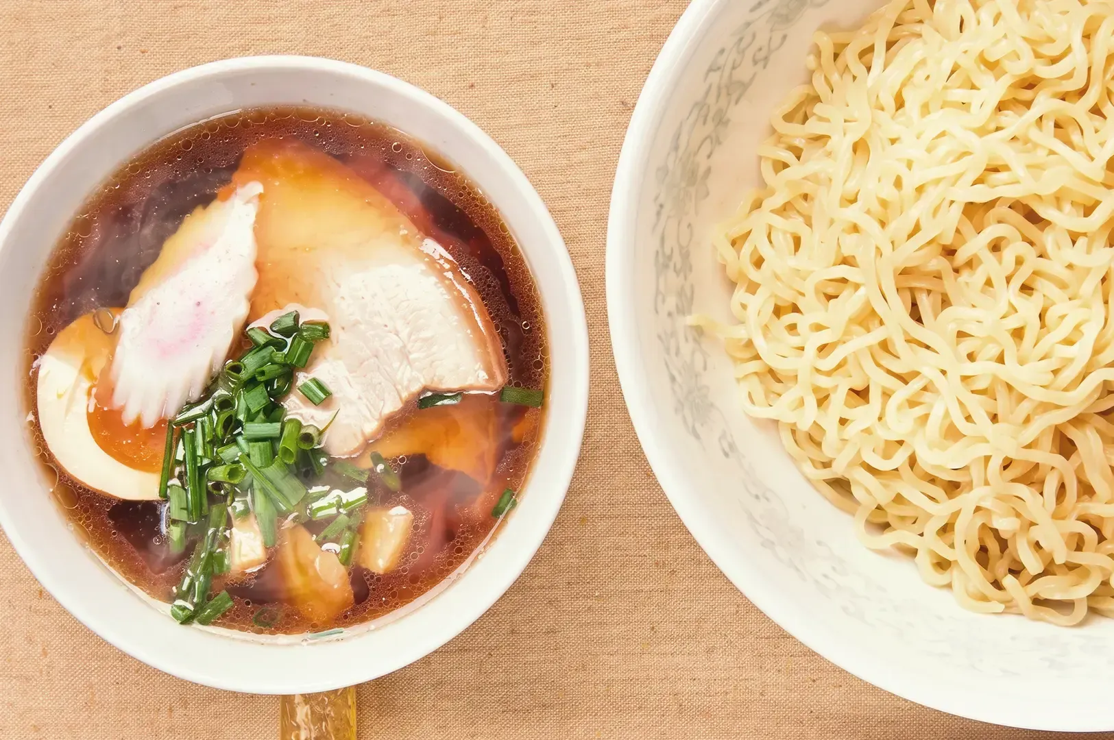 Top view of ramen broth with egg, pork meat and veggie toppings beside cooked noodles