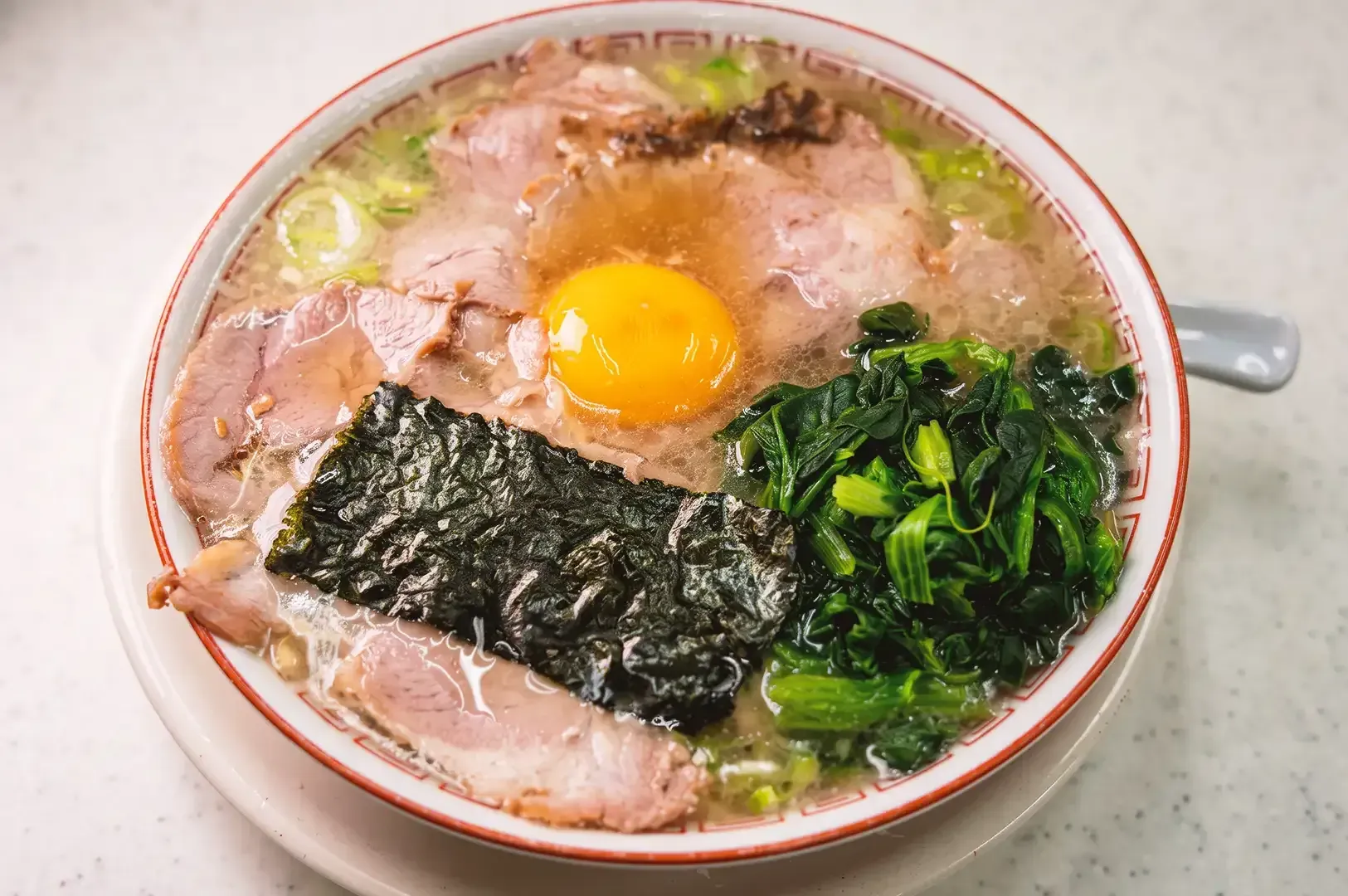 Close up of big japanese ramen bowl filled with seaweed, pork meat slices, egg yolk and vegetables