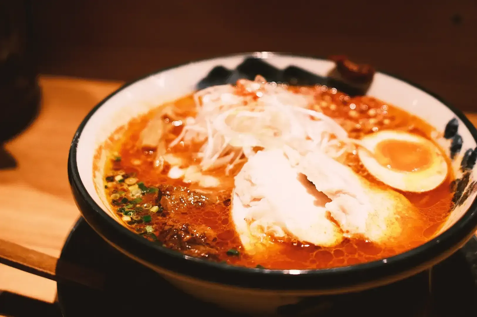 Bowl of ramen with egg, pork meat, shredded vegetable and bits of spring onions on a rich broth