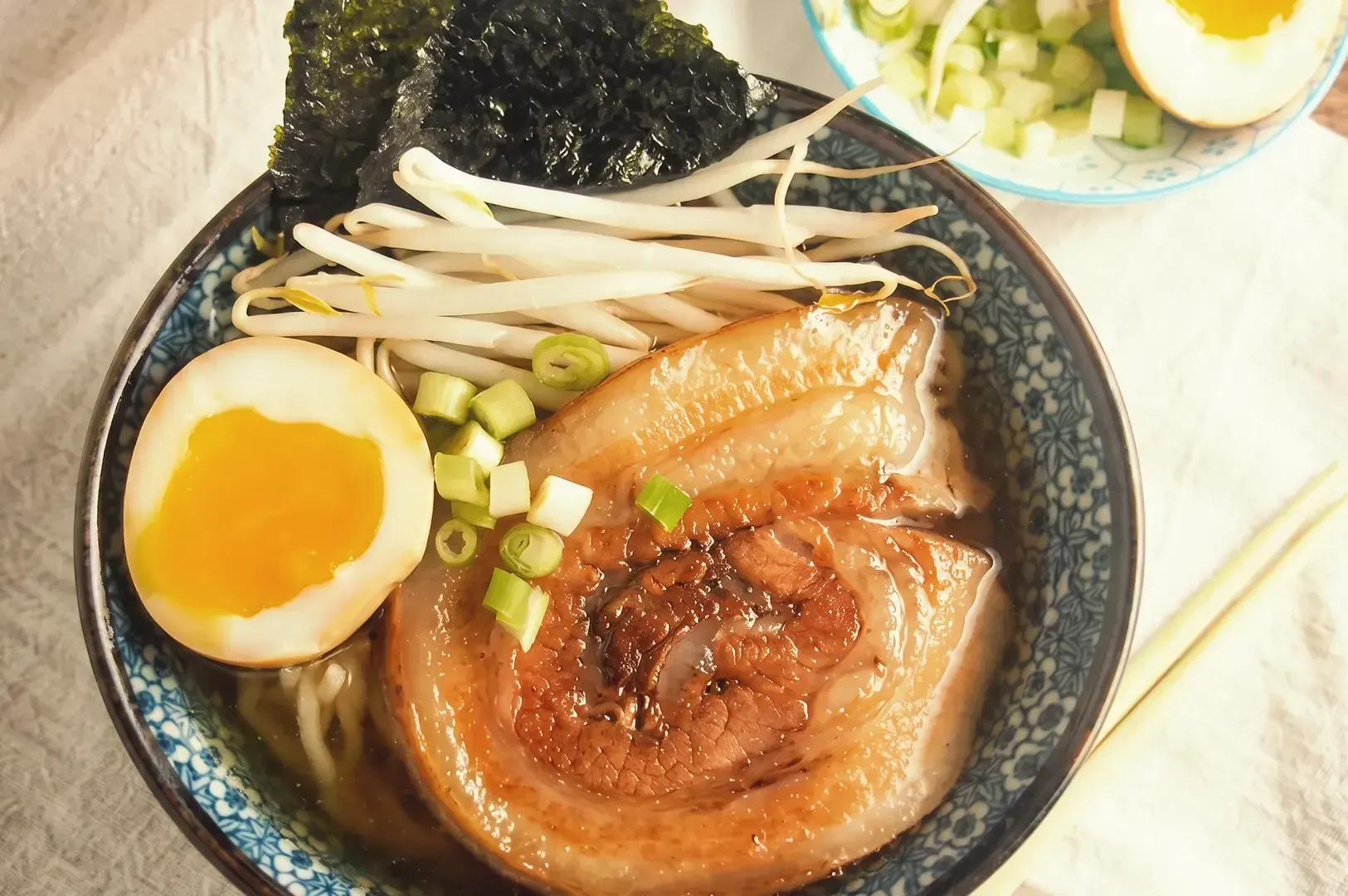A bowl of ramen with pork meat, beansprouts, spring onions and egg toppings