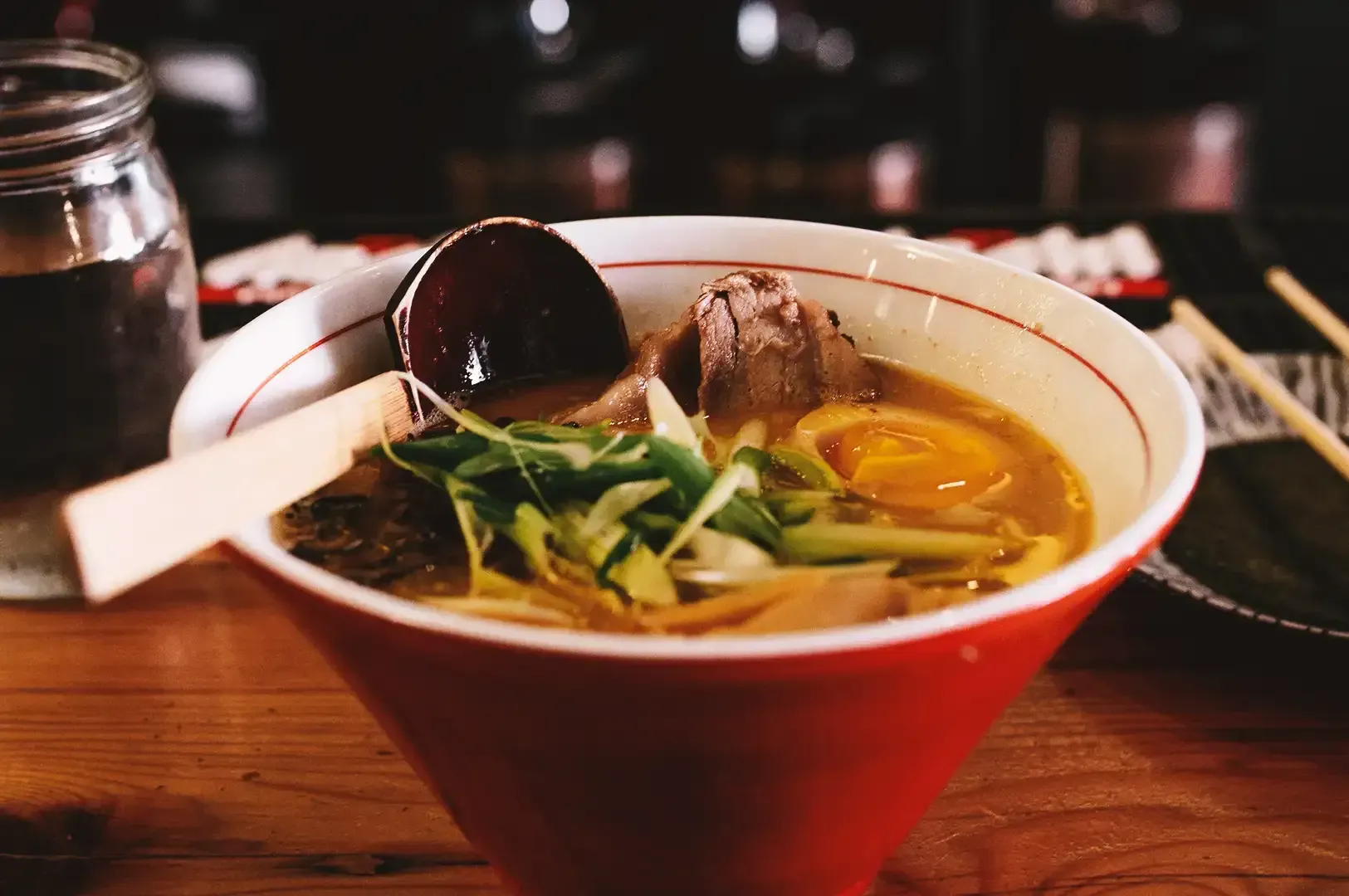 Close up of ramen with sliced vegetables, pork meat, egg and rich broth in a red bowl