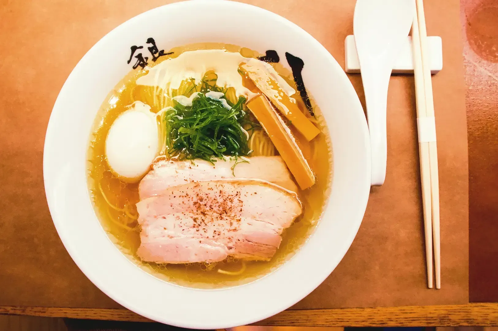 Top view of ramen broth topped with pork meat, egg, vegetables with utensils on right side