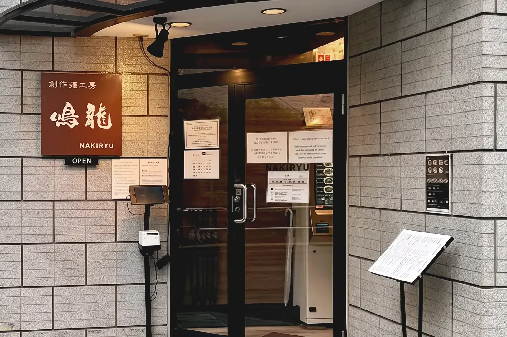 Modern storefront of Nakiryu Ramen with brown wooden signage written with Japanese letters and paper