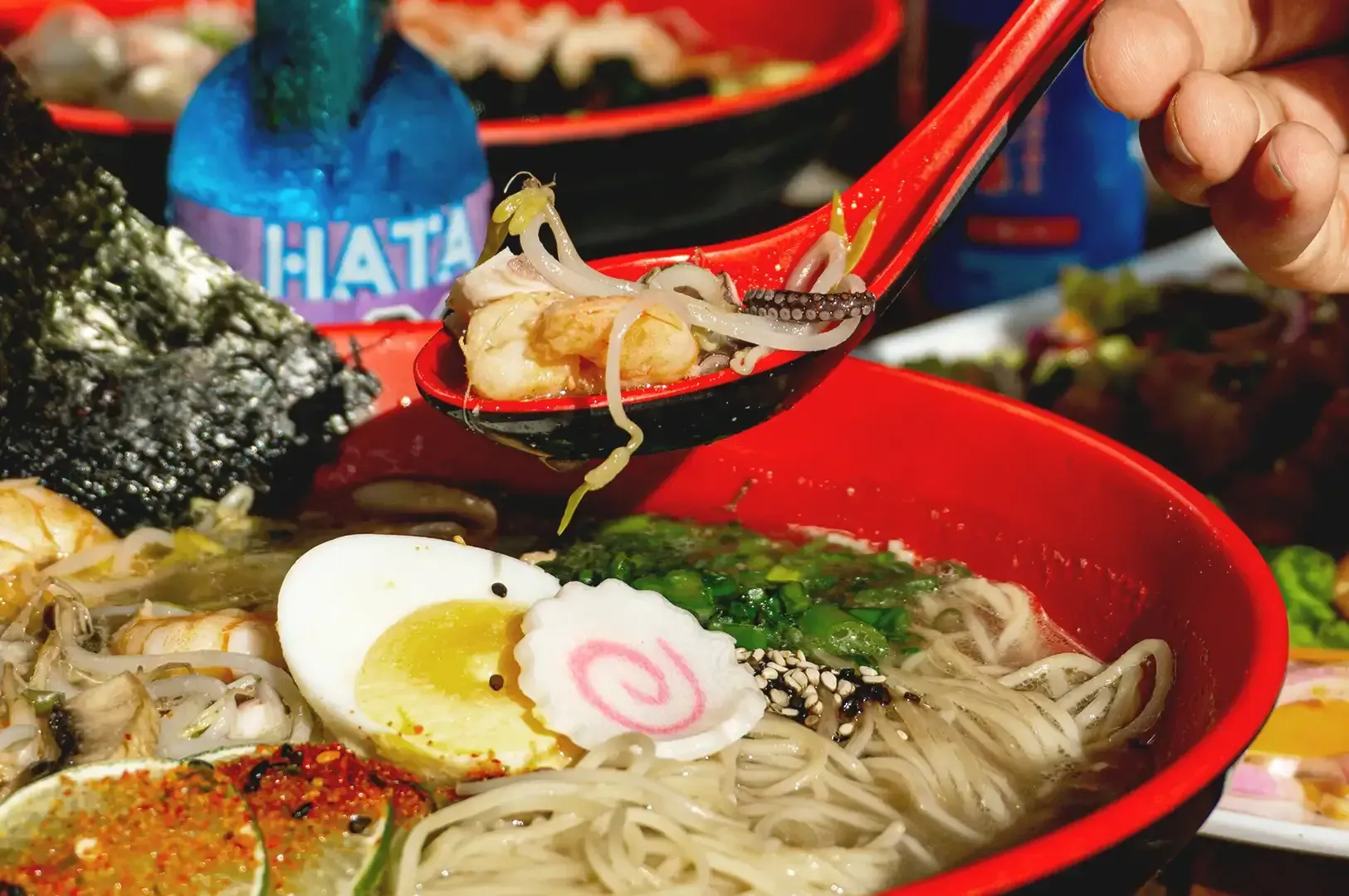 Spoon scooping a portion from the ramen bowl topped with egg, lime, mushroom, and seaweed