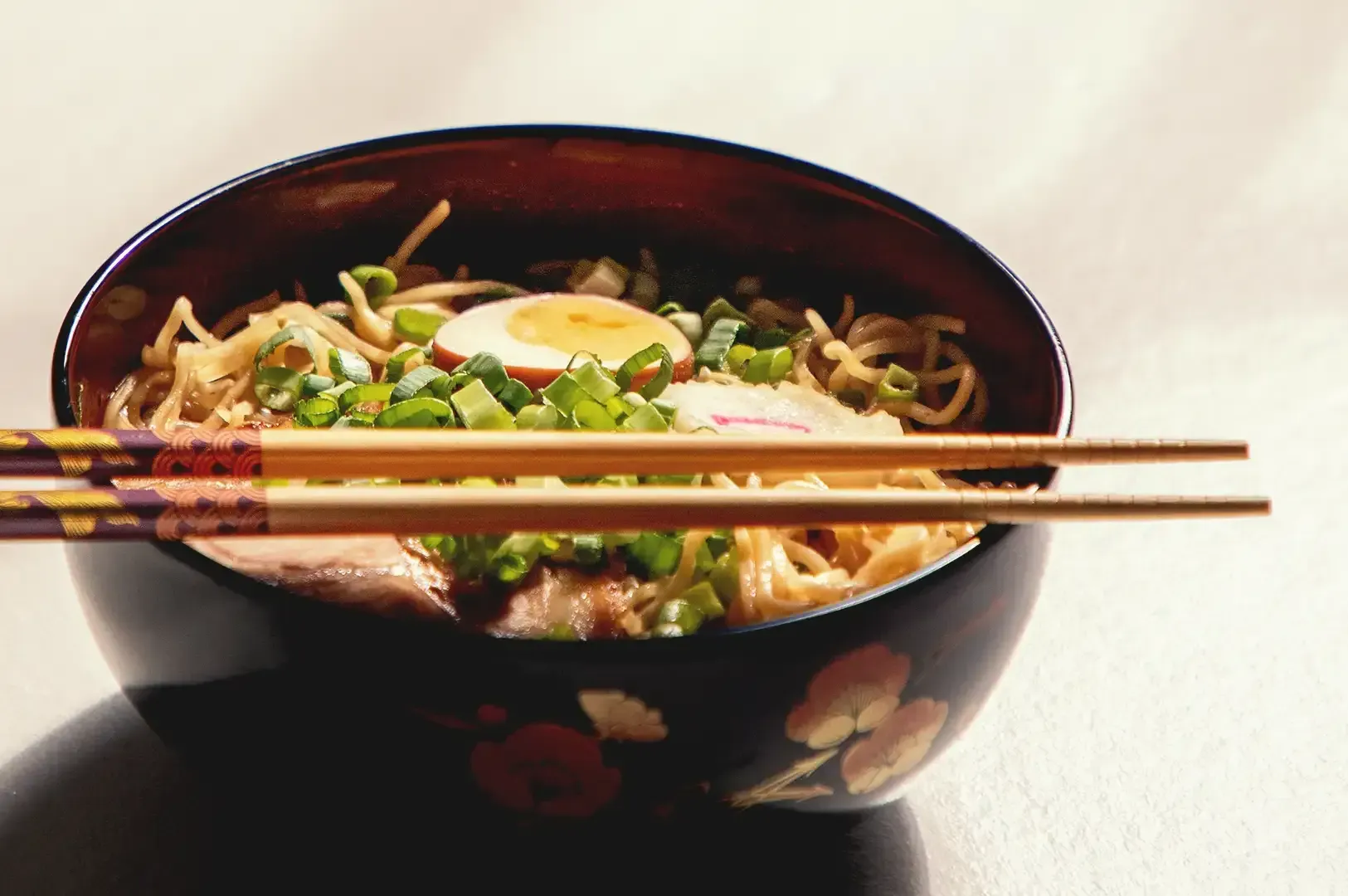 Ramen noodles with egg and pork meat garnished with spring onions in a black bowl with chopsticks