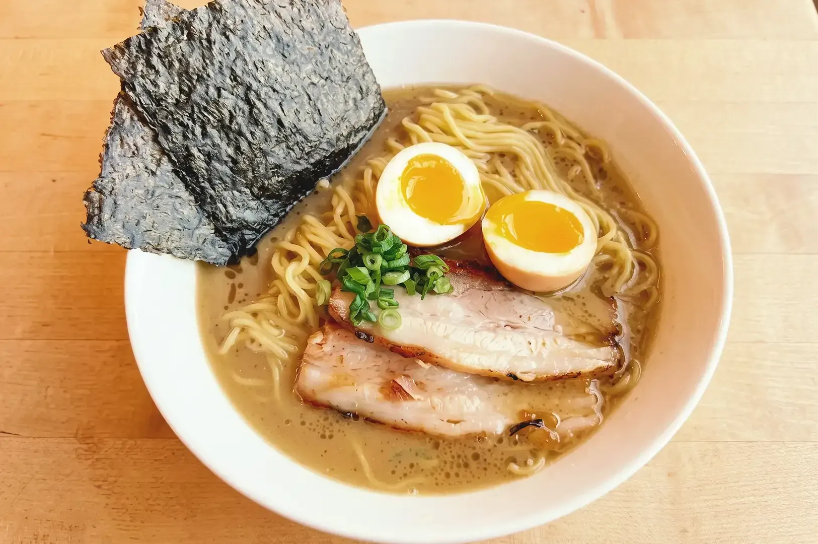 Ramen noodles topped with chashu, boiled eggs, spring onions and seaweed in a white bowl