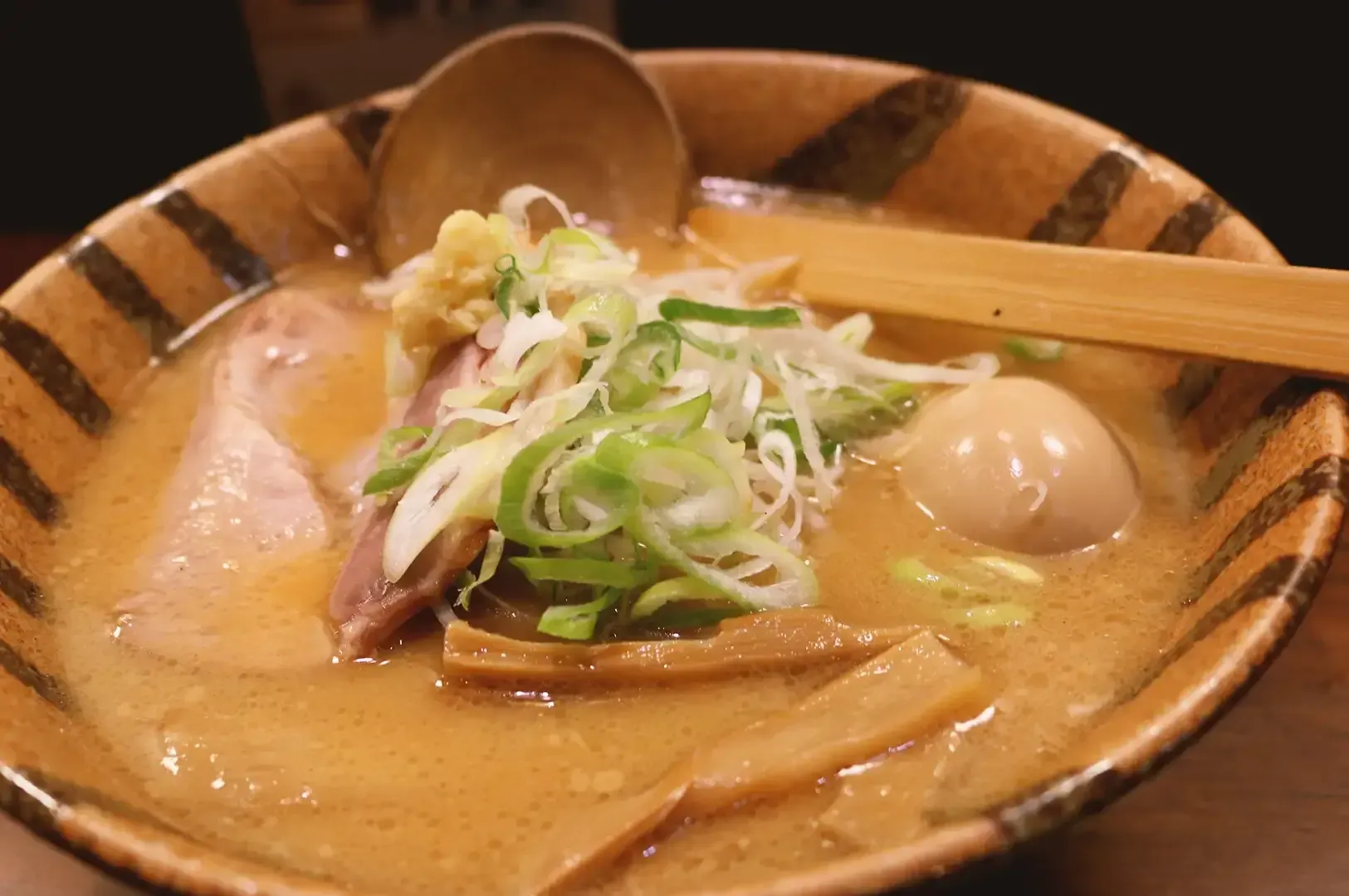 Ramen noodles composed of noodles, egg, chashu and mushroom garnished with spring onions with a wood