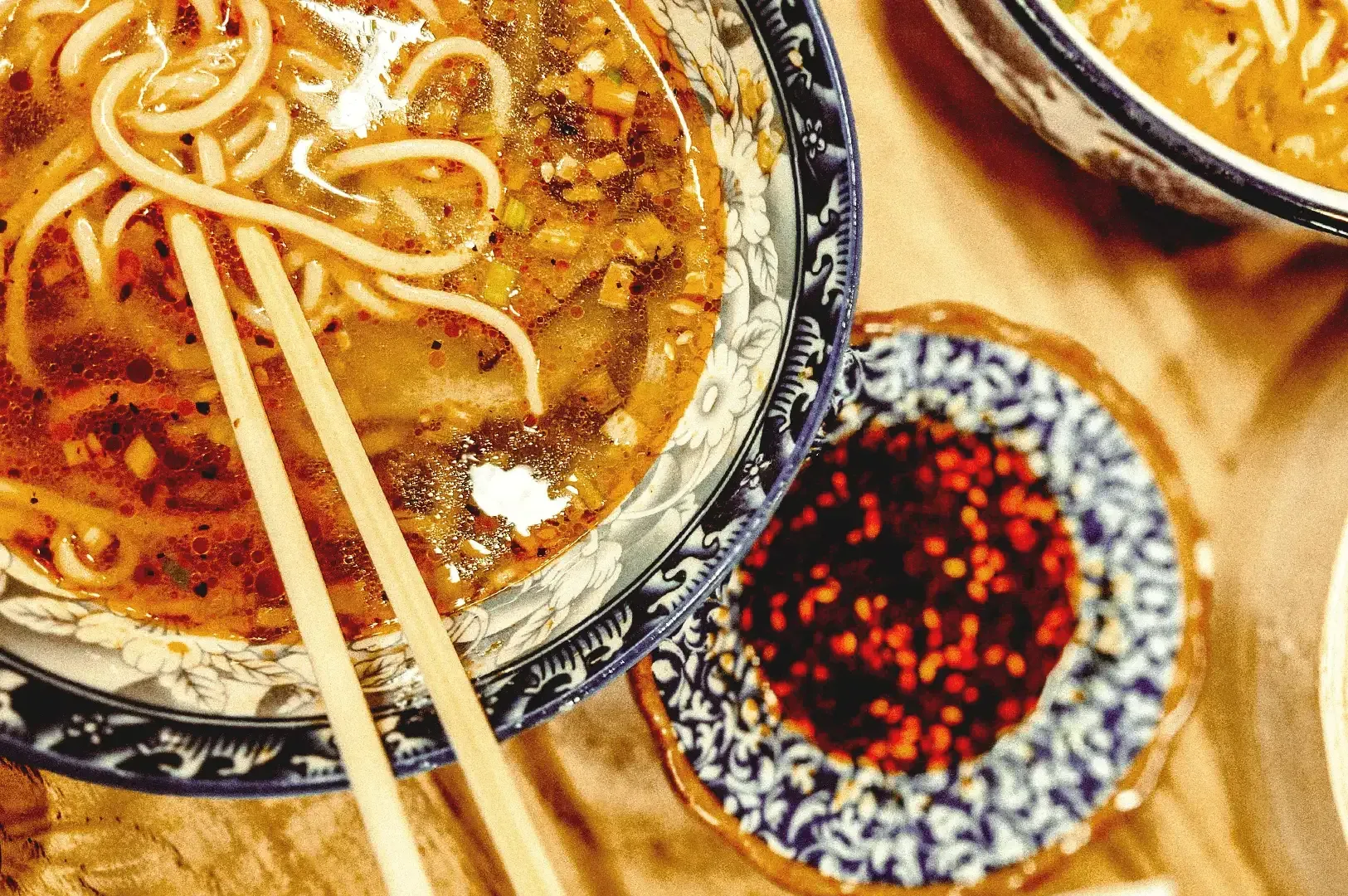 Ramen noodles drenched in seasoned broth in an antique bowl beside a small plate of red chili oil