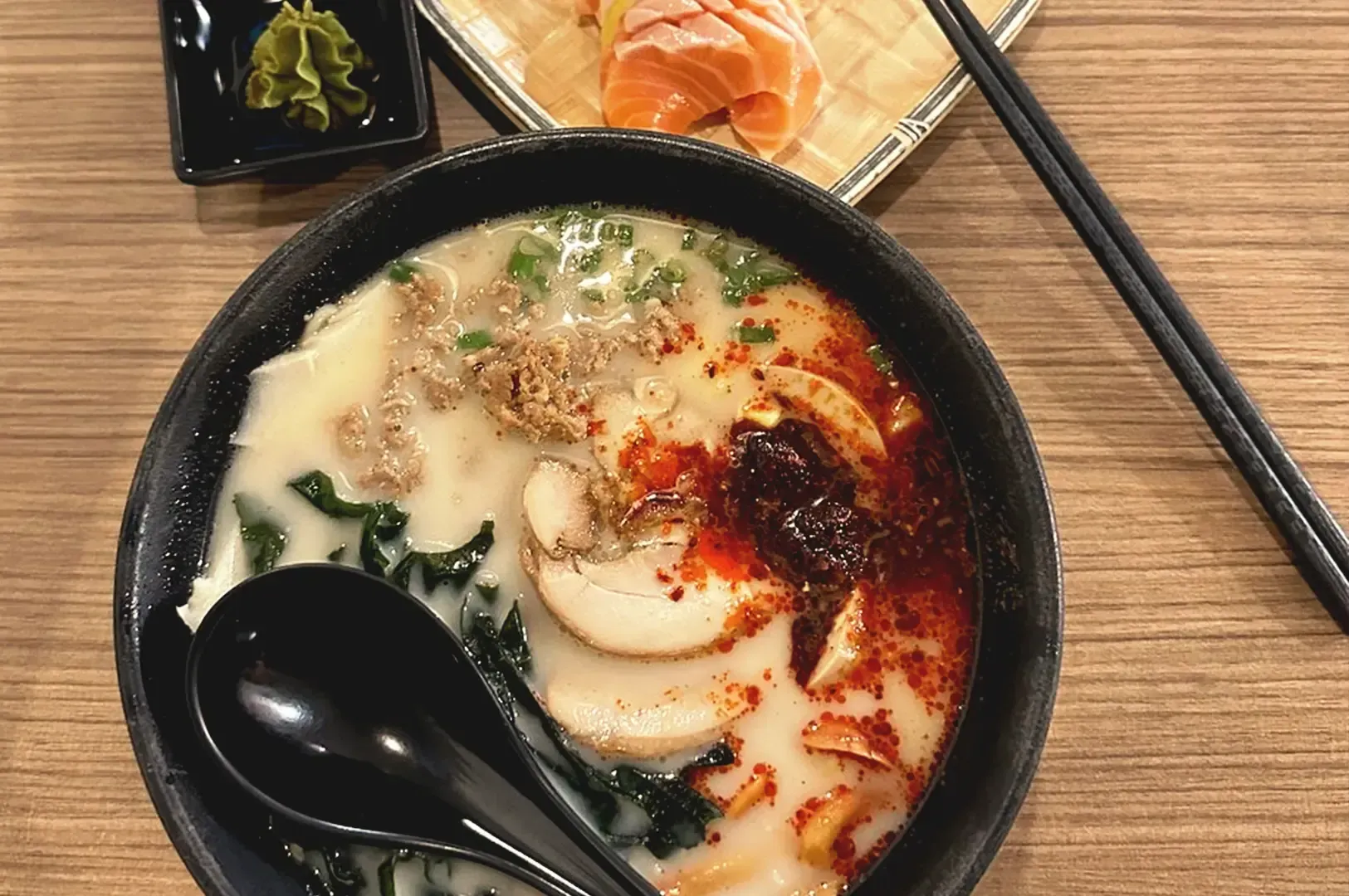 Top view of creamy ramen broth seasoned with chili oil, pork meat, seaweed and spring onions in black bowl