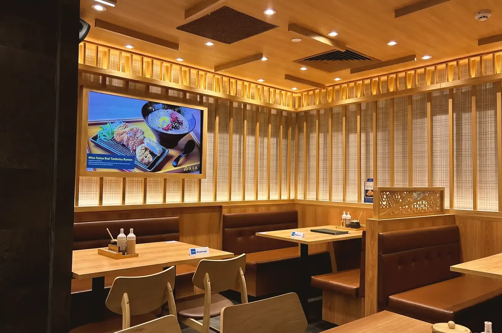 Interior of Tonkatsu ENbition following traditional japanese design using wooden materials and a TV displaying promotional dishes