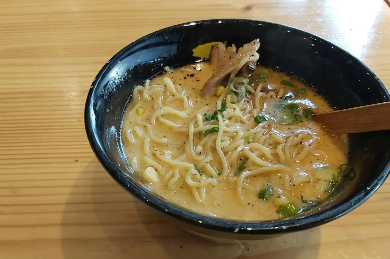 Creamy ramen in black bowl with pork and green onions on wooden table