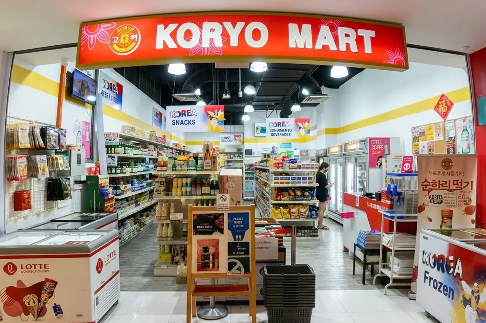 Koryo Mart Korean grocery store entrance in Singapore featuring bright red signage, organized aisles with Korean snacks, beverages, frozen products, and customer shopping inside