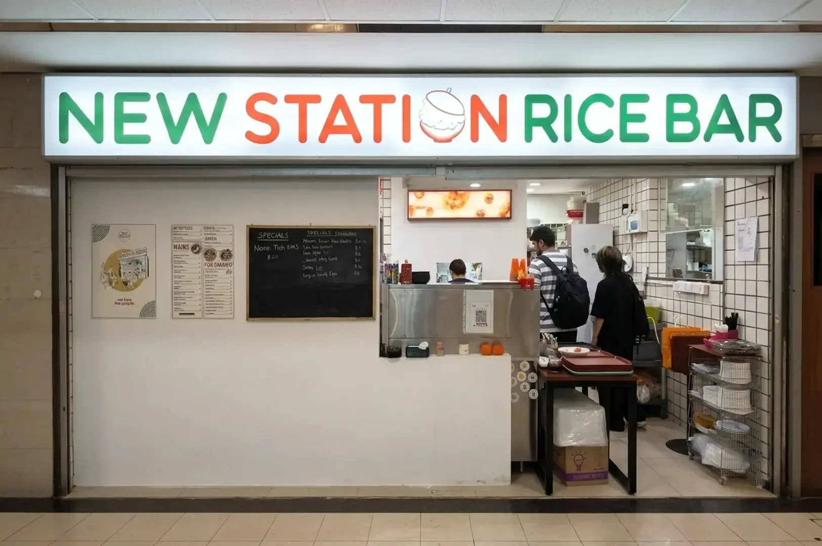 New Station Rice Bar storefront with illuminated sign and customers ordering at counter