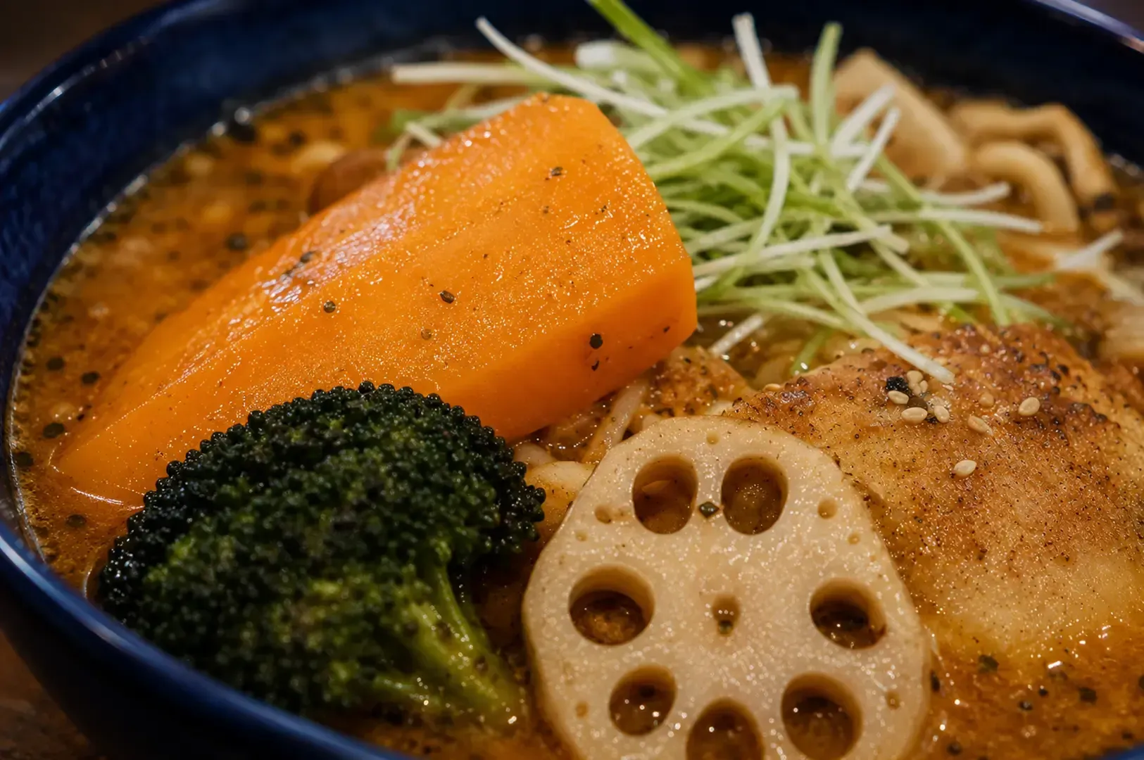 Close-up of a hearty soup curry bowl featuring large chunks of carrot, broccoli, lotus root, and meat in a rich broth