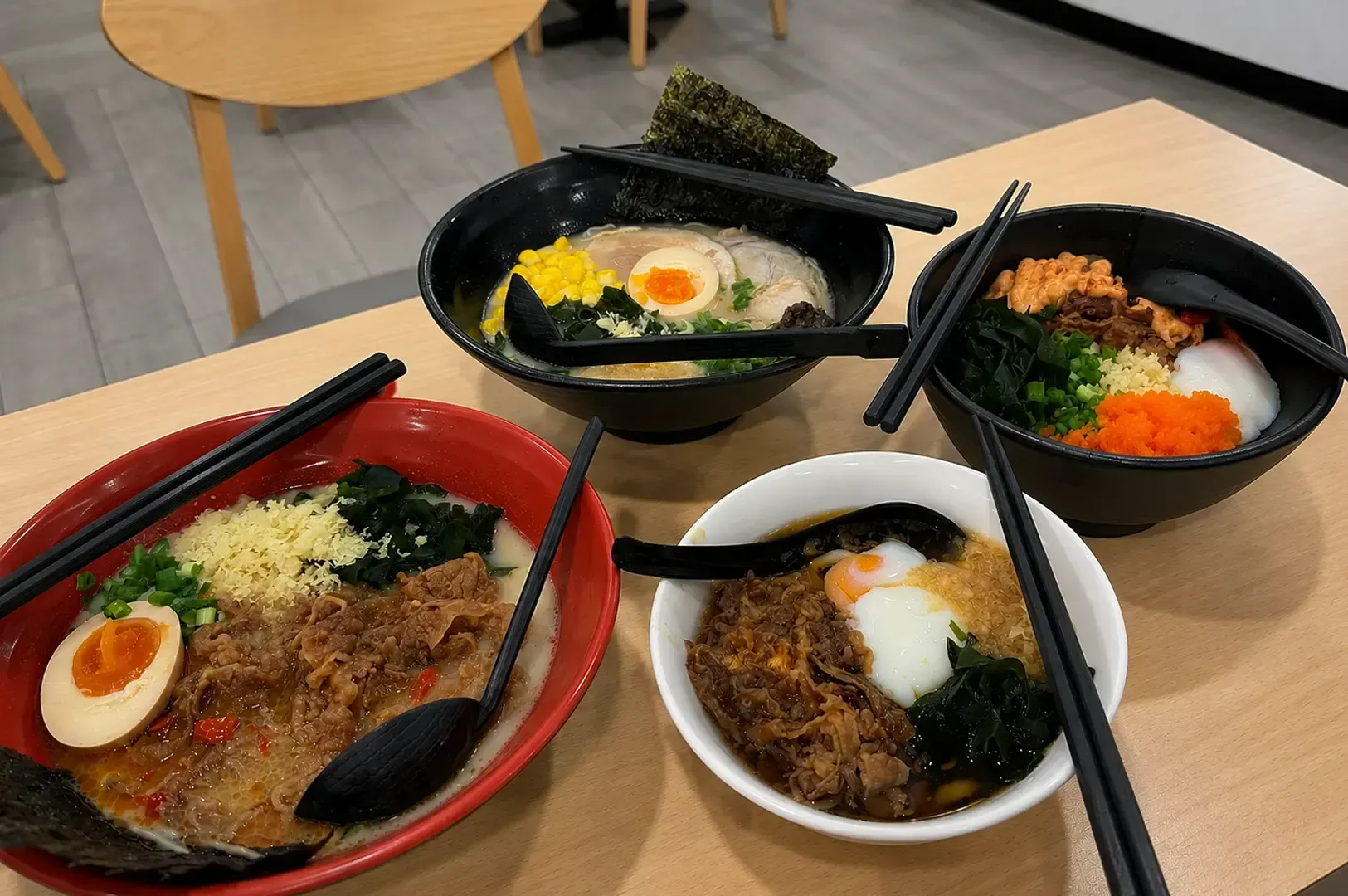 Table spread of four Japanese noodle dishes including ramen with corn and egg, beef udon, and gyudon bowls topped with various ingredients like seaweed and roe