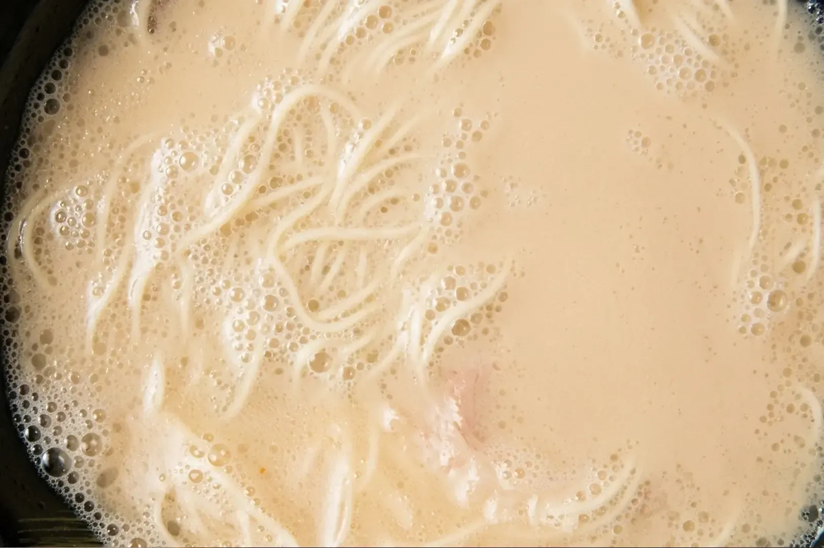 Close-up top-down view of rich, milky Tonkotsu broth with noodles visible underneath