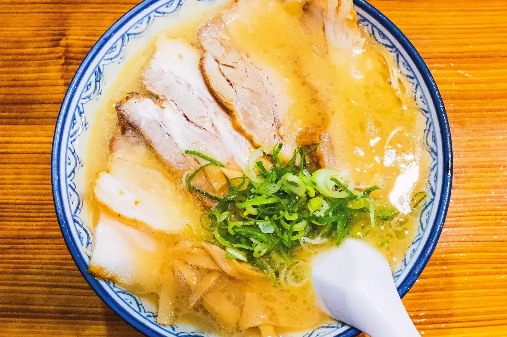 Top view of ramen bowl containing rich ramen broth, slices of pork meat and egg garnished with spring onion